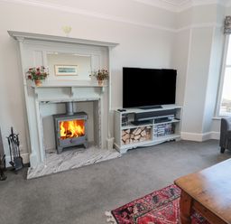 A living room with a fireplace TV stand with a TV and firewood and a coffee table at Whinstones at 4 The Villas in Embleton