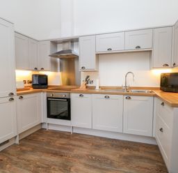 A kitchen with wooden countertops white cabinets a sink an oven and under cabinet lighting at Lakeside Village Lodges & The Potting Shed in Capesthorne near Macclesfield