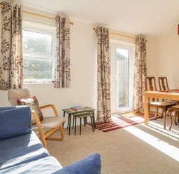 A living room with blue sofa beige chair wooden dining table with four chairs and floral curtains at Rowan Cottage in St Bees