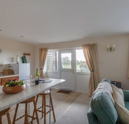 A kitchen and living area with a countertop and stools and a sofa near a door with curtains at Willow Barn in Cucklington near Wincanton