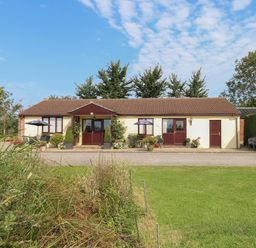 A single story house with brown roof and cream walls with garden and patio furniture outside at Willow Barn in Cucklington near Wincanton