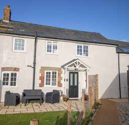 A front view of a white cottage with black door and outdoor seating on a paved path at Willowbrook Cottage in Litton Cheney