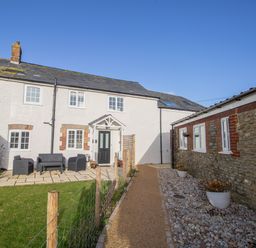 An outdoor patio area with garden chairs and a table next to a white cottage and a stone building at Willowbrook Cottage in Litton Cheney