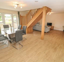 A dining area with a glass table and six gray chairs next to a staircase with a living room in the background at Woodpecker Barn in Hensol near Pontyclun