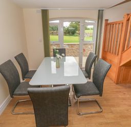 A dining area with a glass table surrounded by six chairs next to a wooden staircase and a window with a view outside at Woodpecker Barn in Hensol near Pontyclun