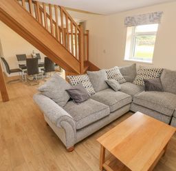 A living room with a gray sectional sofa and wooden coffee table below a staircase and a dining table with chairs at Woodpecker Barn in Hensol near Pontyclun