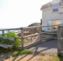 An outdoor seating area with wooden chairs and table near a house with open doors overlooking the sea at The Reach in Hallsands