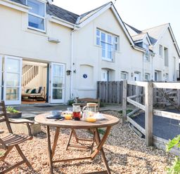 A patio area with a round wooden table and two wooden chairs outside a row of white houses at The Reach in Hallsands