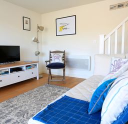 A living room with a sofa a chair a TV on a stand and framed pictures on the wall at The Reach in Hallsands