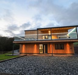 A modern two-story wooden house with glass balcony and outdoor lights at Fron Haul - Robin Goch in Llanfwrog near Ruthin
