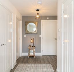 A hallway with white doors a small wooden table with a lamp and a round mirror on a gray wall at Beacon House in St Agnes