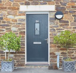 A front door with the number 24 flanked by two potted plants on a stone wall at Beacon House in St Agnes