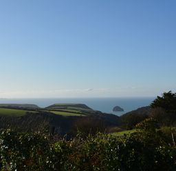 A coastal landscape with green fields bushes and the sea in the distance at Glenhaven in Trewarmett near Tintagel