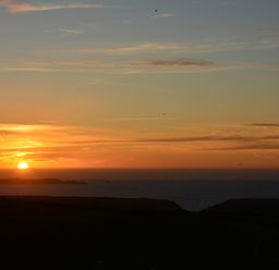 A sunset over the ocean with a mostly clear sky and some clouds at Glenhaven in Trewarmett near Tintagel