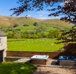 A garden with two hot tubs next to a stone house and a field with sheep at Oakdene Country House in Sedbergh
