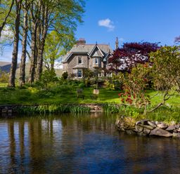 A stone house with a pond lawn chairs and trees at Oakdene Country House Sedbergh