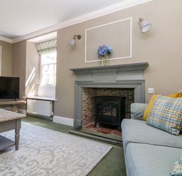 A living room with a fireplace, a light blue sofa with patterned cushions, a wooden coffee table, and a television at Culdrose Manor in Helston