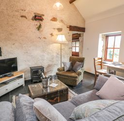 A living room with a grey sofa armchair rustic coffee table and TV at Nyth Y Wennol in Llanfachraeth