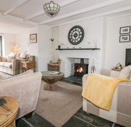 A living room with a stone fireplace clock and couches with a yellow blanket at Hawthorn Cottage in St Teath