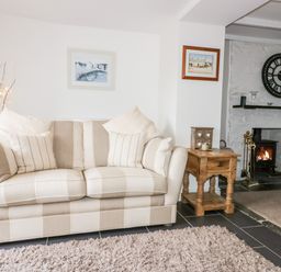 A living room with a beige striped sofa wooden side table and a fireplace with a large clock on the wall at Hawthorn Cottage in St Teath