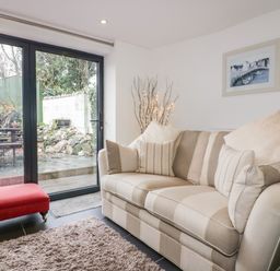 A living room with a striped sofa cushions a red bench shaggy rug and glass doors leading outside at Hawthorn Cottage in St Teath
