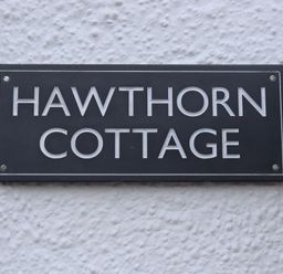 A black and white sign reading hawthorn cottage on a textured white wall at Hawthorn Cottage in St Teath