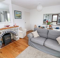 A living room with a gray sofa and stone fireplace adjacent to a dining area set with dishes at Valley High in Solva