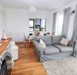 A living room with a gray sofa next to windows with striped curtains a dining table set for four and a fireplace with a model sailboat at Valley High in Solva