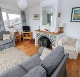 A living room with grey sofas a white armchair a stone fireplace TV and wooden furniture at Valley High in Solva