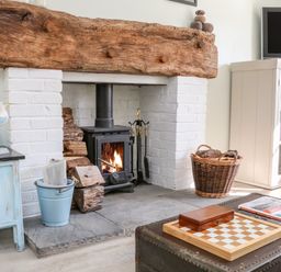A fireplace with a wood stove surrounded by logs and tools next to a blue cabinet and a white bookshelf at 3 Elm Cottage in Carhampton