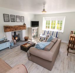 A living room with a fireplace a sofa striped armchairs a television and a small dining table at 3 Elm Cottage in Carhampton