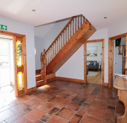 A hallway with tiled floor wooden staircase and a wooden console table with a lamp at SeaShells in Castlerock