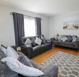 A living room with three sofas a patterned rug a lamp curtains and a wall painting at SeaShells in Castlerock