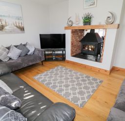 A living room with two gray sofas a television a fireplace and a rug on a wooden floor at SeaShells in Castlerock