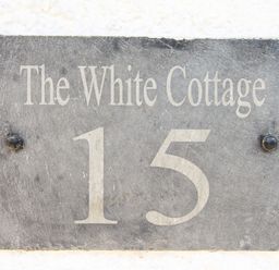 A house number plaque with the text The White Cottage 15 on a white wall at The White Cottage in Weymouth