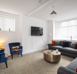 A living room with gray sofas and blue armchairs with floral cushions at The White Cottage in Weymouth