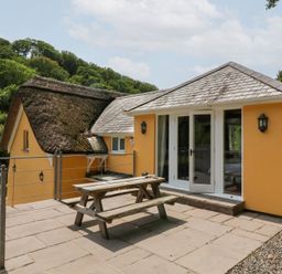 An outdoor area with a thatched roof and a garden table at Old Maids Cottage in Woolacombe