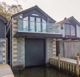 A waterfront property with stone walls and glass balconies over a dock at The Boat House at Louper Weir in Bowness-On-Windermere