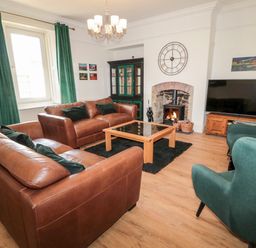 A living room with brown leather sofas green armchairs a fireplace and a TV at The Old Sweet Shop in Alnwick