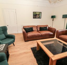 A living room with brown leather sofas green chairs a wooden coffee table and green curtains at The Old Sweet Shop in Alnwick