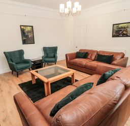 A living room with two brown leather sofas two green armchairs a wooden coffee table and framed pictures on the walls at The Old Sweet Shop in Alnwick