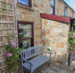 A stone cottage exterior with a wooden bench and flowering climbing plants on trellises at Inglenook Cottage Broad Haven