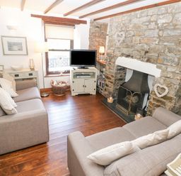 A living room with two gray sofas a stone fireplace a television on a cabinet and wooden flooring at Inglenook Cottage Broad Haven