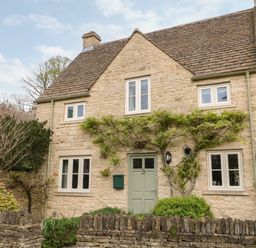 A stone house with green door and windows with plants on the facade at 3 Painters Field in Quenington Near Cirencester