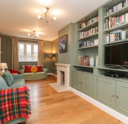 A living room with sofas a fireplace built in shelves with books and a television at 3 Painters Field in Quenington Near Cirencester