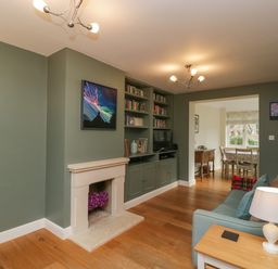 A living room with built in bookshelves and a fireplace leading to a dining area at 3 Painters Field Quenington Near Cirencester