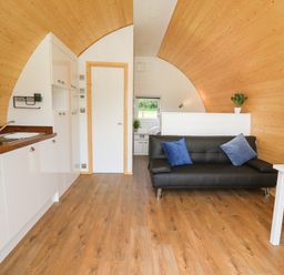 An open plan room with a kitchen area on the left a black sofa with blue cushions and a white dining table with chairs at Seren in Llandrindod Wells
