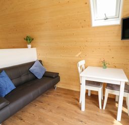 A small room with a brown sofa blue cushions a white table with two chairs and a wall-mounted television at Seren in Llandrindod Wells
