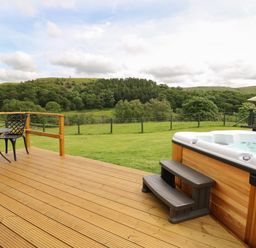 A wooden deck with a hot tub a small round table with two chairs and green hills in the background at Seren in Llandrindod Wells