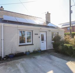 A small house with solar panels on the roof and potted plants by the door at Tanyfron Holiday Studio in Bryngwran near Gwalchmai